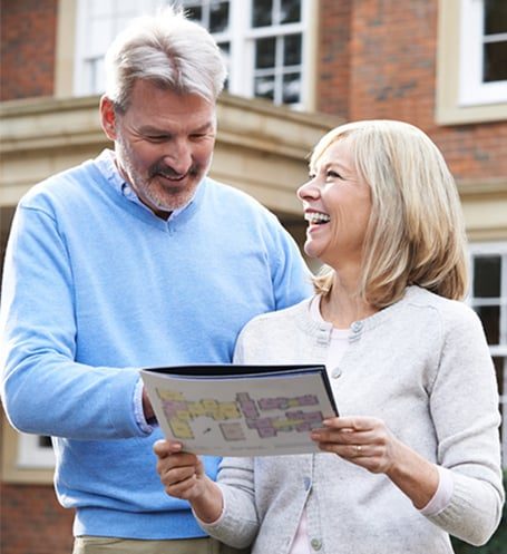 Mature Couple Standing Outside House Looking At Property Details — Seniors Real Estate in Gold Coast, QLD
